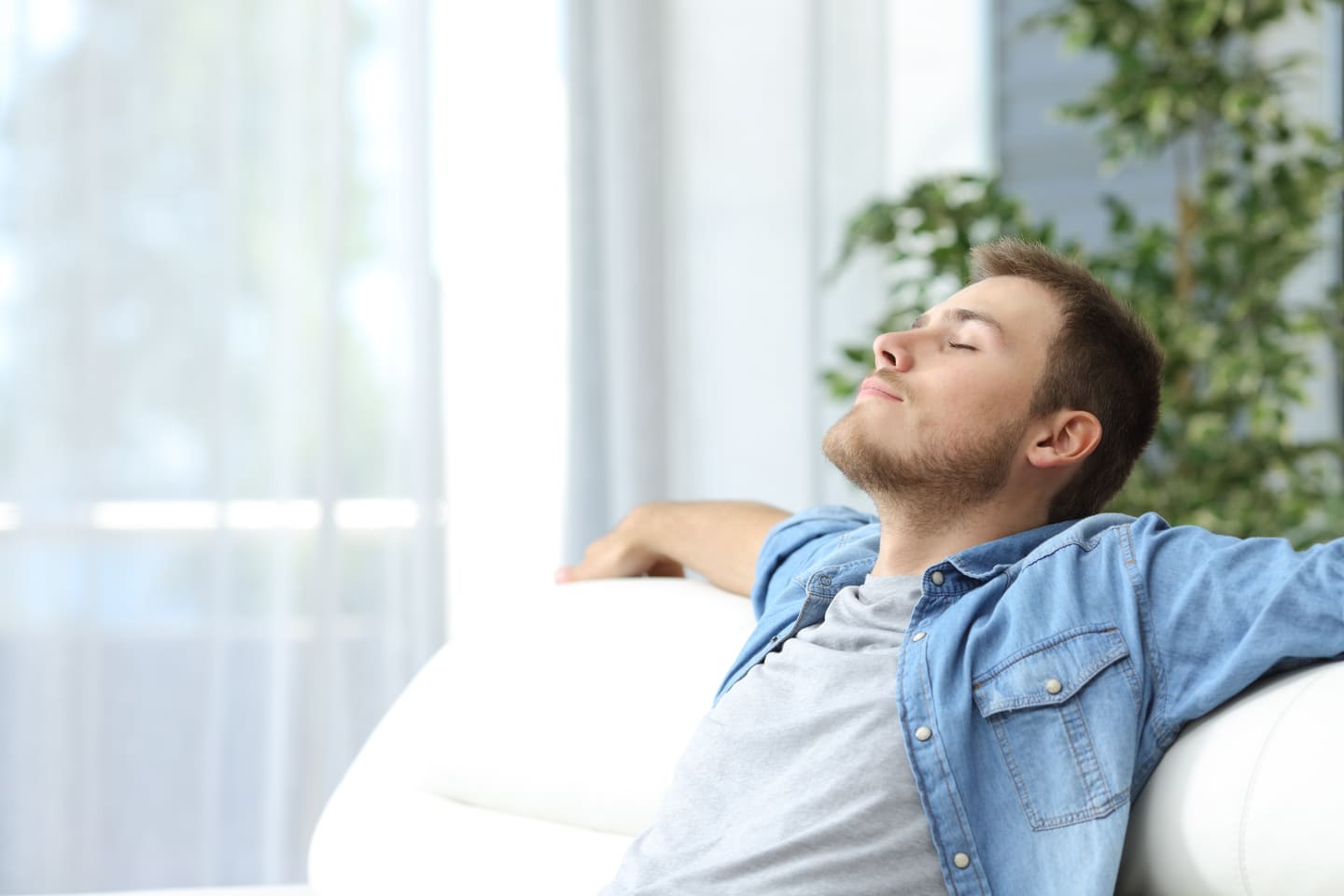 Hombre sentado en sofá respirando - Beneficios de las construcciones ecológicas - Cuidado del medio ambiente